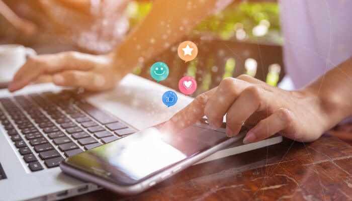 Closeup of a woman's hand while she works on fractional marketing on a laptop and texts on a phone.
