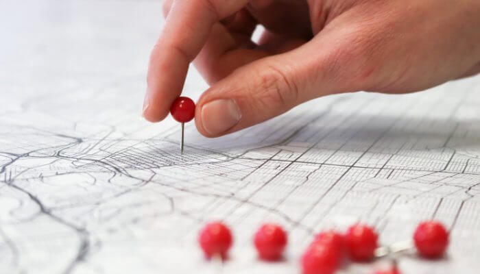 Closeup of hand placing a red pin on a street map to show a multi-location business.